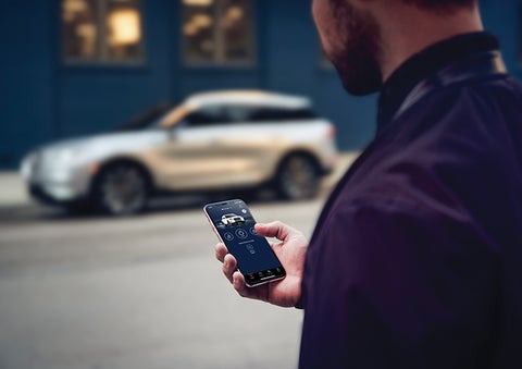 A person is shown interacting with a smartphone to connect to a Lincoln vehicle across the street. | Lexington Park Ford Lincoln in California MD