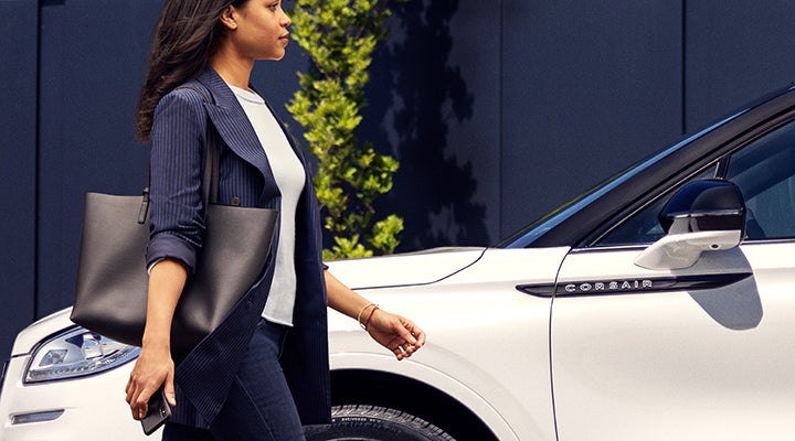 A woman approaches a 2024 Lincoln Corsair® SUV while holding a smartphone. | Lexington Park Ford Lincoln in California MD
