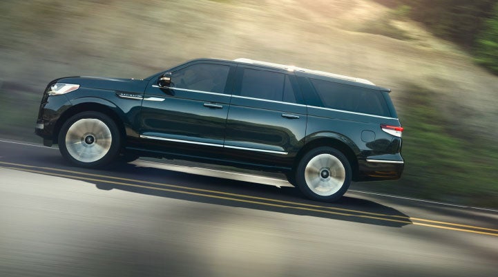 A 2024 Lincoln Navigator® SUV being driven on a freeway bathed in sunlight.