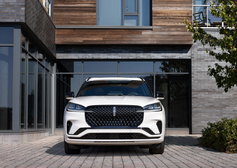 A white 2025 Lincoln Aviator® SUV is shown parked outside a modern building with gray brick and wood accents. | Lexington Park Ford Lincoln in California MD