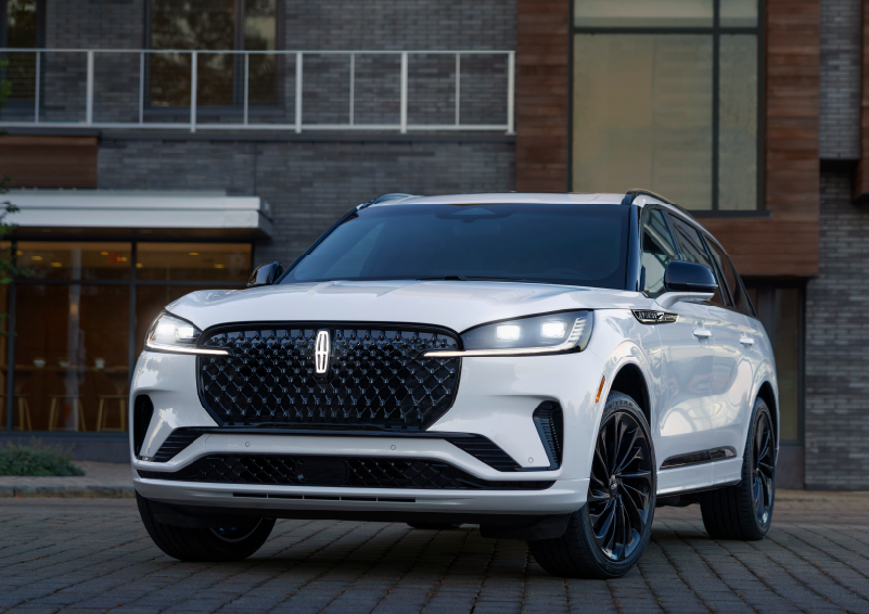 A white 2025 Lincoln Aviator® SUV is shown parked outside a modern building with gray brick and wood accents. | Lexington Park Ford Lincoln in California MD