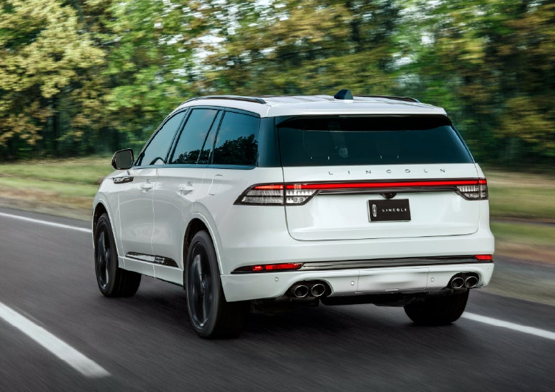 A white 2026 Lincoln Aviator® SUV is being driven away down a road lined with colorful trees. | Lexington Park Ford Lincoln in California MD