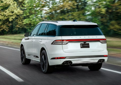 A white 2026 Lincoln Aviator® SUV is being driven away down a road lined with colorful trees. | Lexington Park Ford Lincoln in California MD