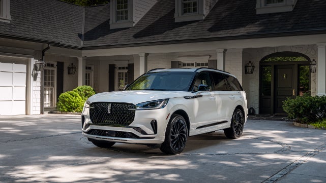A white 2026 Lincoln Aviator® SUV is parked in the driveway of a luxury home. | Lexington Park Ford Lincoln in California MD