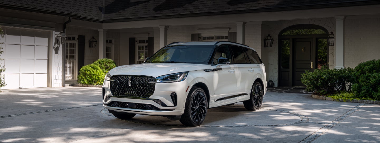 A white 2026 Lincoln Aviator® SUV is parked in the driveway of a luxury home. | Lexington Park Ford Lincoln in California MD