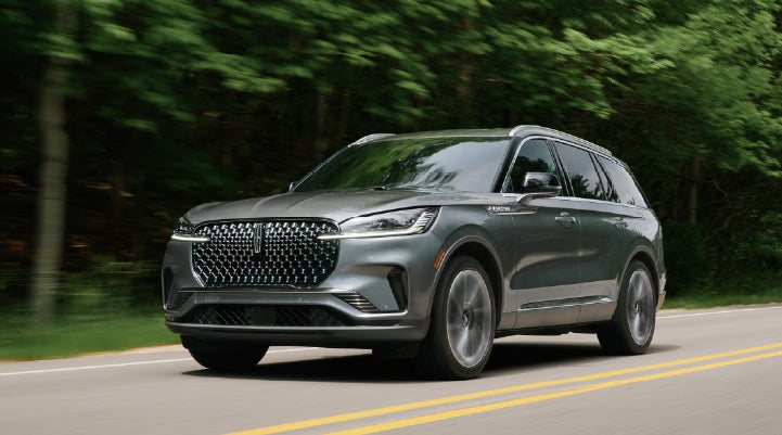 A 2027 Lincoln Aviator® SUV is being driven down a road lined with trees. | Lexington Park Lincoln in California MD